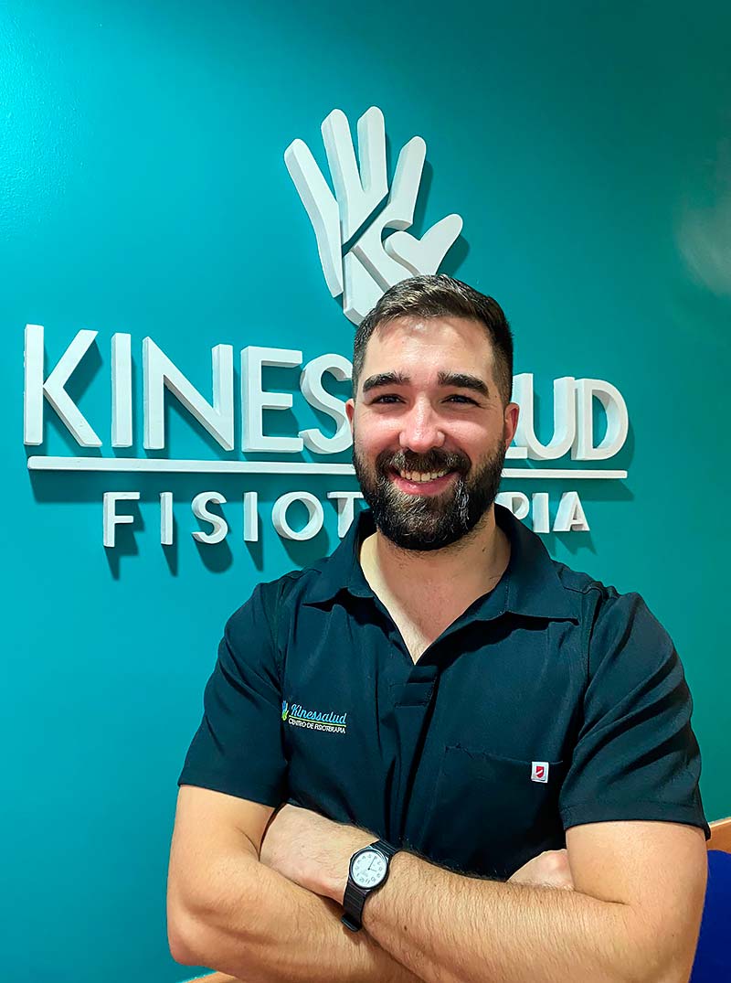 Hombre con barba frente a una pared que dice Kinessalud Fisioterapia.